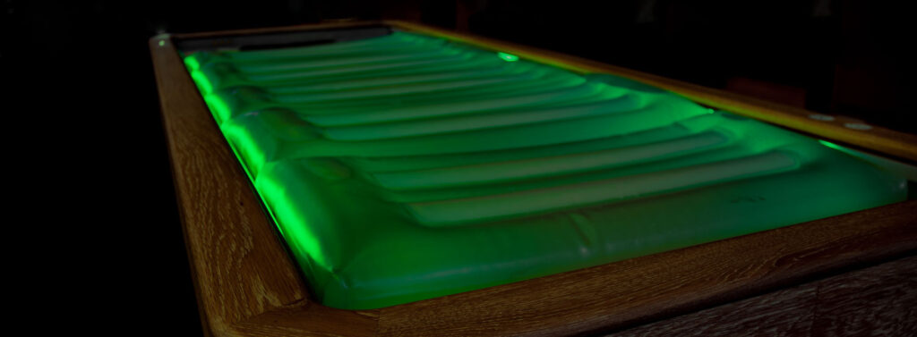 Alt-Text: "Illuminated luxury spa treatment table with green LED lights, Gharieni."