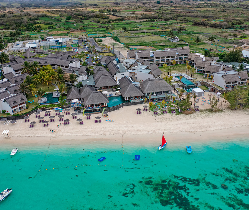 Aerial view of luxury beachfront resort with turquoise waters and red sailboat.