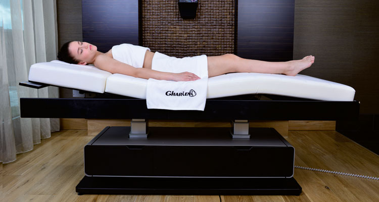 A woman relaxing on a Gharieni premium treatment table in a luxurious spa setting.