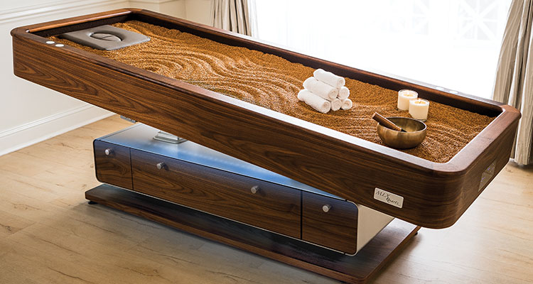 Luxurious Gharieni spa table with sand, candles, and towels for premium treatments.