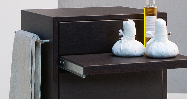 Modern spa equipment with dark wood finish, oil bottle, and herbal compresses.