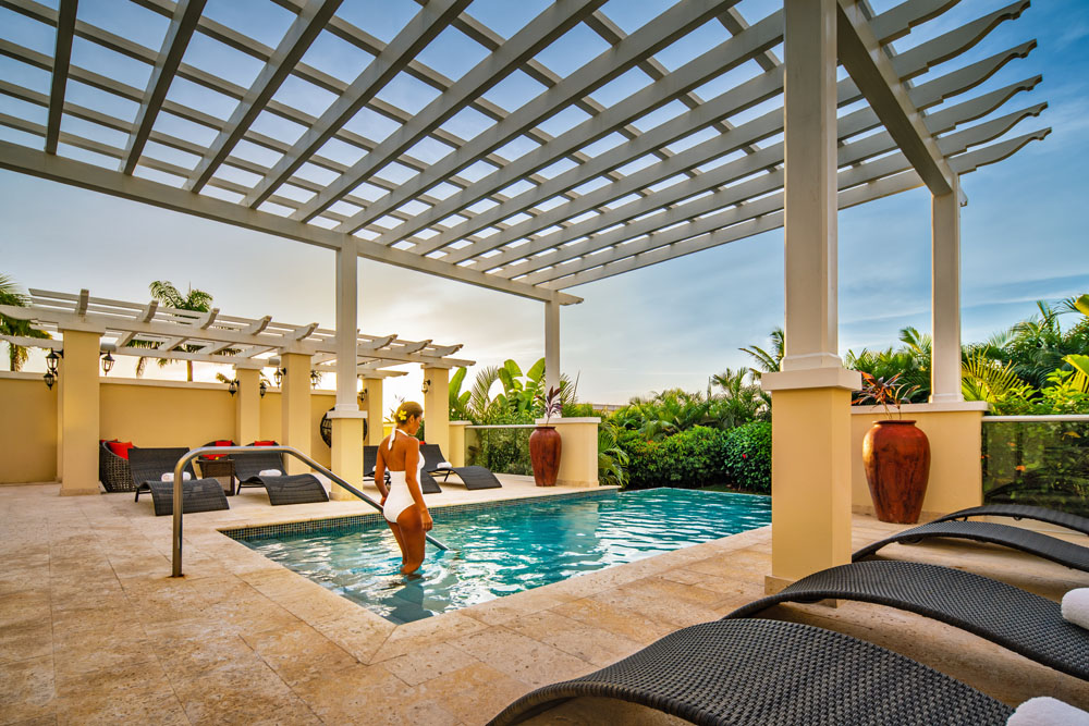 Luxurious spa setting with a pool and treatment tables under a pergola.