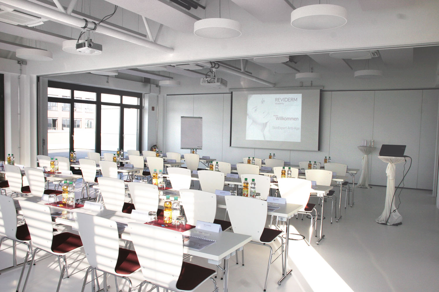Modern conference room with white chairs, tables set for a premium spa equipment seminar.