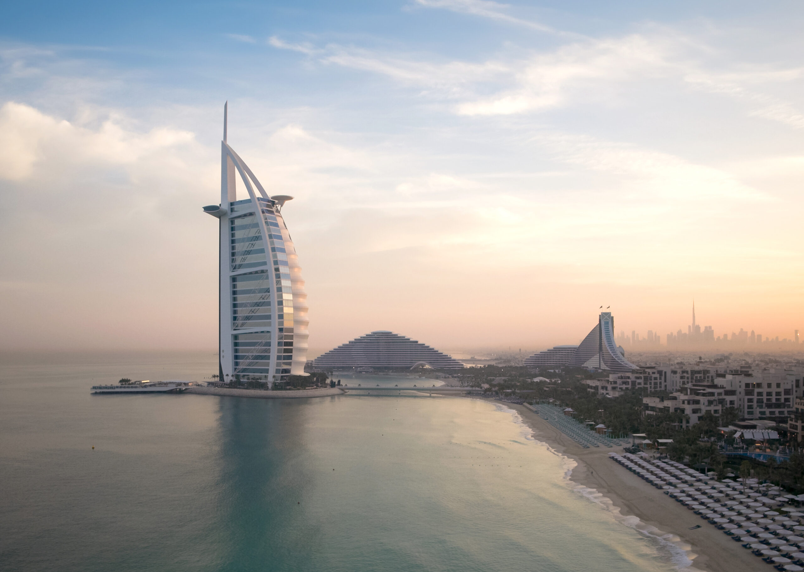 Skyline of Dubai with iconic luxury hotel by the sea at sunset.